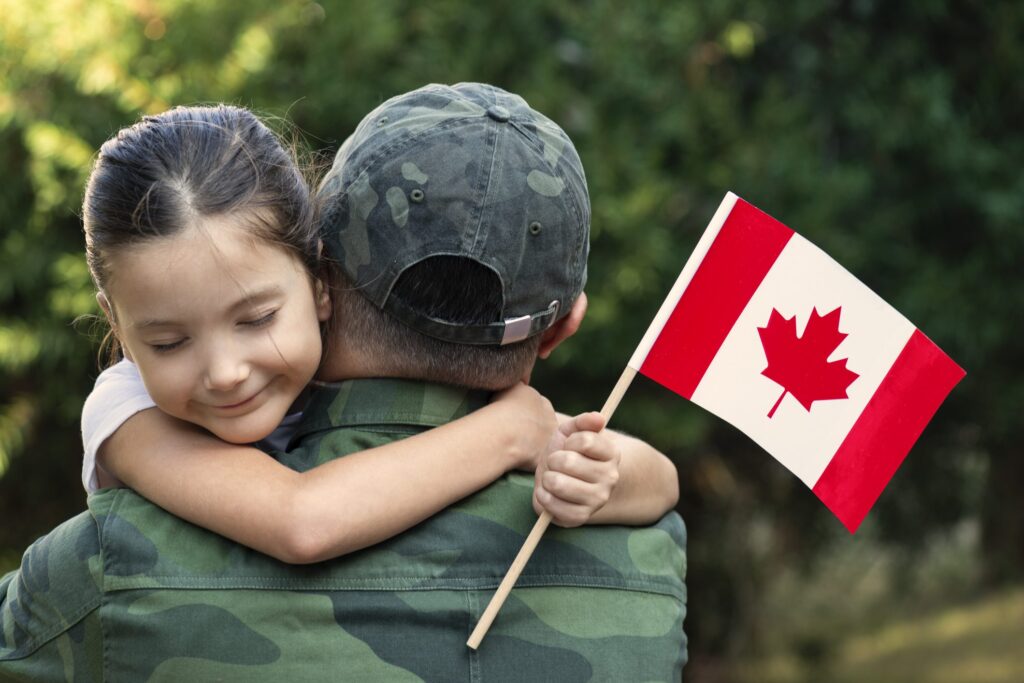 Little girl hugs the soldier father and holding Canadian flag. | Une petite fille embrasse le père soldat et tient le drapeau canadien.