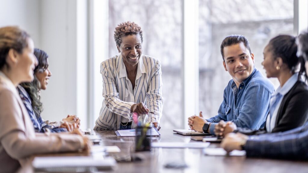 A diverse group of individuals engaged in conversation while seated around a table in a collaborative setting.