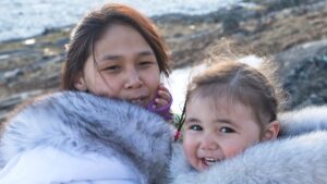 Inuit mother and daughter in fur coats posing on a sea side