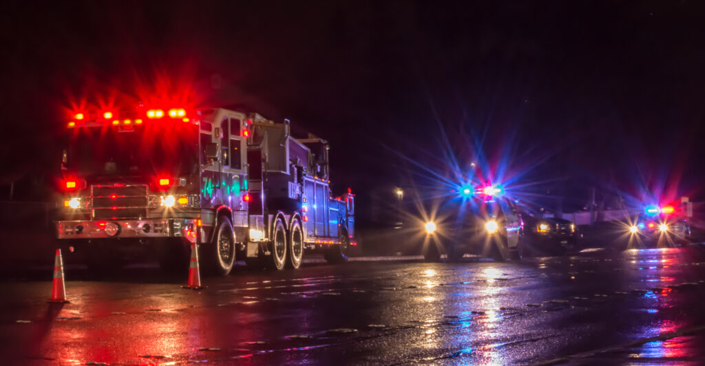 Fire trucks illuminated at night, reflecting on a wet road, showcasing emergency response in a rainy environment.