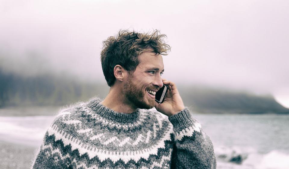 A man wearing a sweater is engaged in a conversation on his cell phone, appearing focused and attentive.