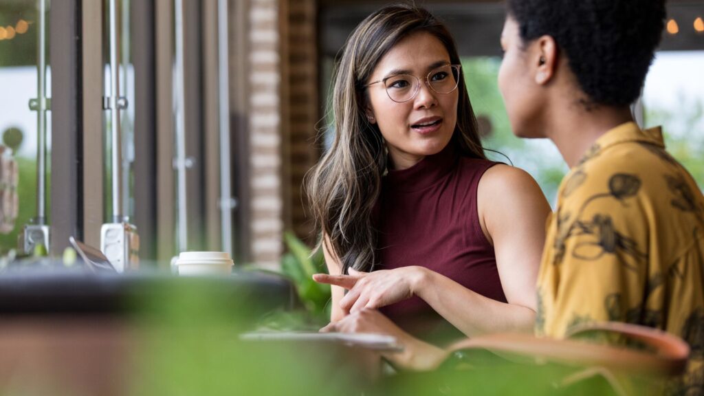 A woman and a man engaged in conversation while seated at a table, sharing ideas and enjoying each other's company.