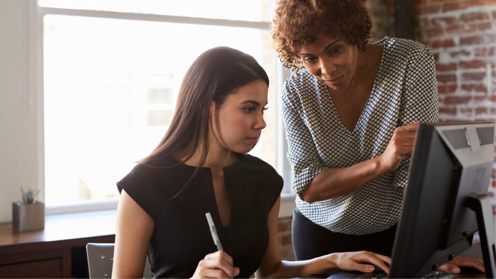 Two women collaborating on a computer, focused on their work and sharing ideas in a professional setting.