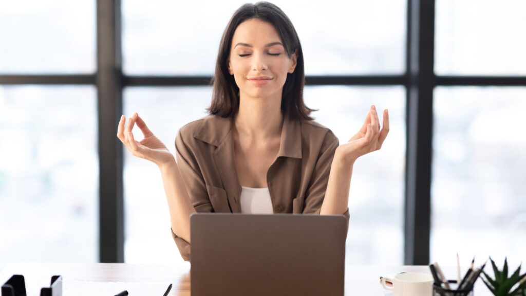A woman in a meditative pose, focused on her laptop, creating a serene atmosphere for mindfulness and concentration.