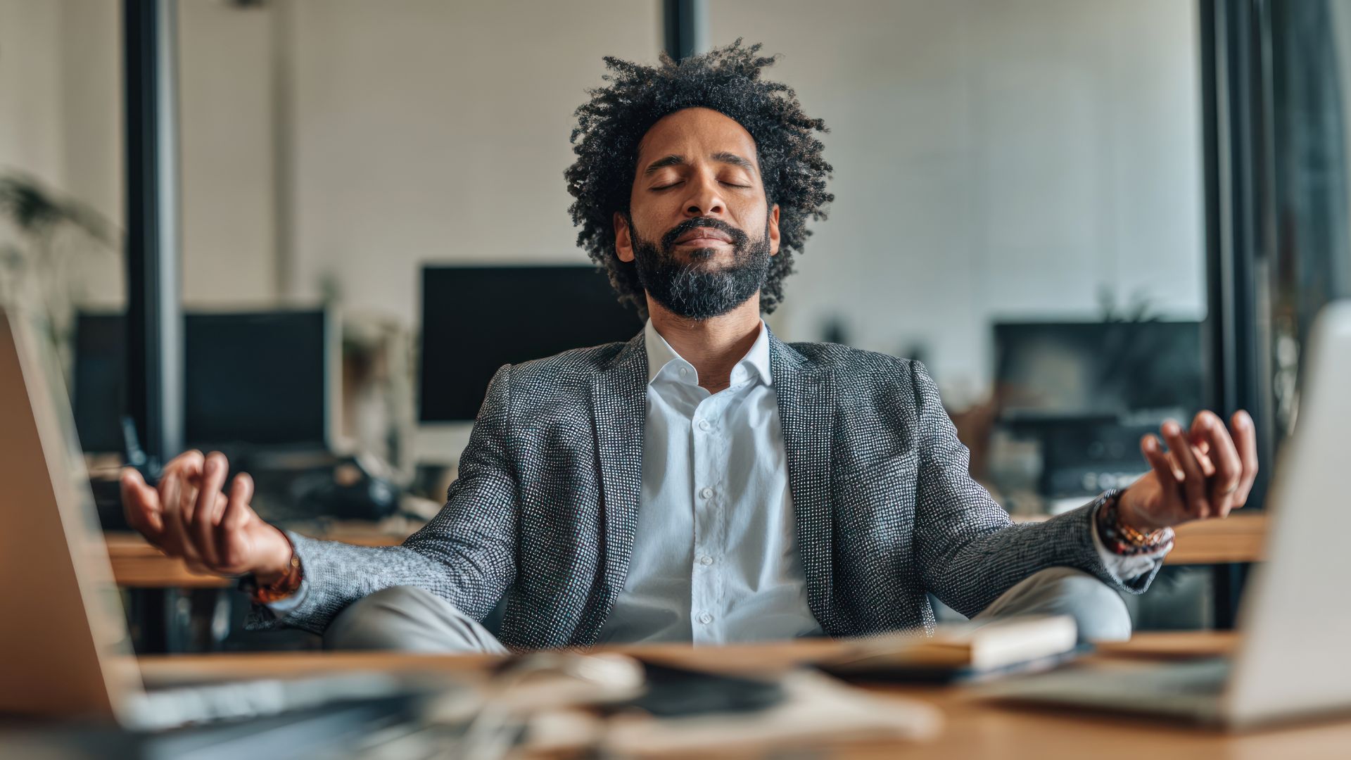 A man meditates calmly in front of his laptop, creating a serene workspace atmosphere.
