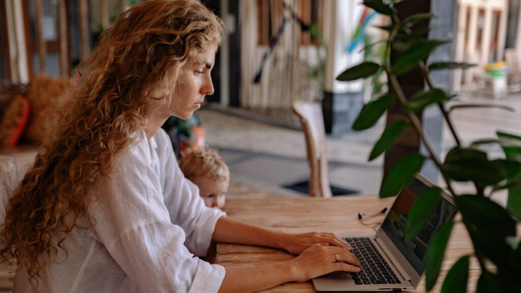 A parent working on a laptop at home with a child nearby, illustrating work-life balance