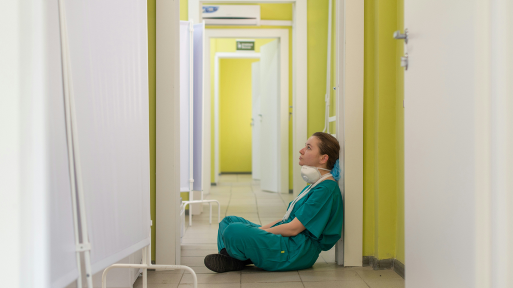 Exhausted healthcare worker in scrubs sitting on a hospital corridor floor