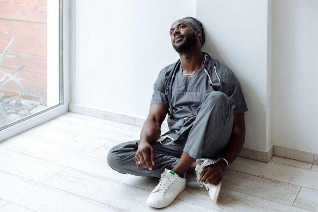 Tired frontline healthcare worker in scrubs resting against a wall after a long shift